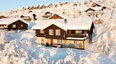 a house covered in snow with houses in the background at Large Cabin With Stunning Views! in Beitostøl