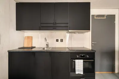 a kitchen with black cabinets and a sink at Comfy studio apartment 200m from bryggen in Bergen