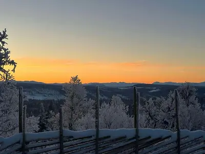 a fence in the snow with the sunset in the background at Family Cabin With Jotunheim Mountain Views in Venabygd