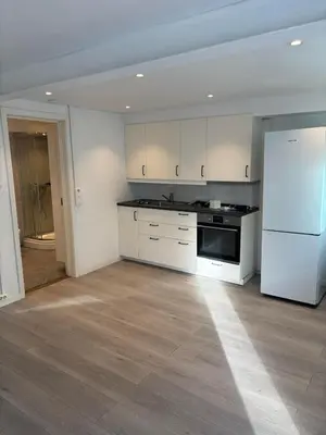an empty kitchen with white cabinets and a refrigerator at studio apartment 24 sqm in Trondheim
