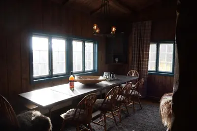 a dining room with a table and chairs and windows at Sjarmerende hytte på Geilo med 5 soverom in Geilo