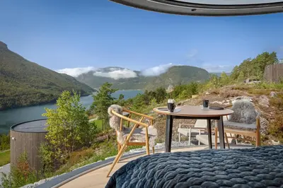 a room with a table and chairs and a view of a lake at The Sognefjord Cabin in Kaupanger