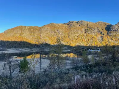 a mountain reflecting in a lake in the middle of a field at 70S Architectural Cabin With Views In Hemsedal in Hemsedal
