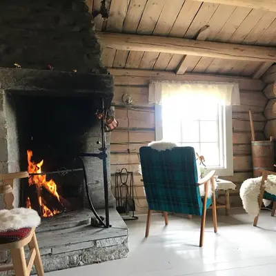 a living room with a fireplace and a chair and a window at Charming lodge from 1888 in Sel