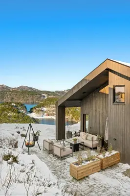 a house on a beach with couches and a table at Cabin Overlooking Ryfylke Fjord in Høyvik