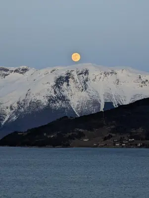a moon over a snow covered mountain with a body of water at Charming guest house with amazing view in Kvam