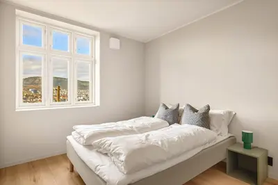 a white bedroom with a bed with white sheets and a window at Stay Panorama - Best view in Bergen l 2BR & Terrace in Bergen