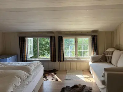 a bedroom with a bed and a couch and two windows at Authentic Norwegian chalet for 8 with fireplaces & modern comfort near Geilo ski slopes in Geilo