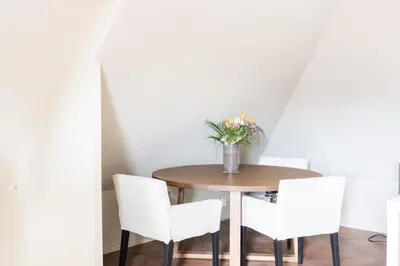 a dining room table with white chairs and a vase of flowers at Large apartment in historical street in Bergen