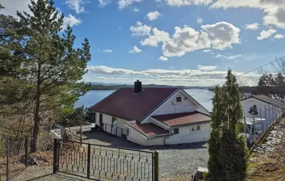 a white house with a brown roof next to the water at Lovely Home In Mosterhamn With Sauna in Mosterhamn