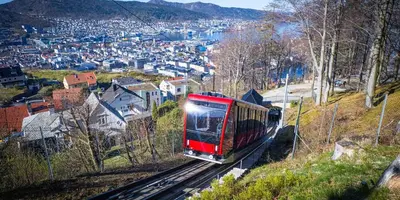 a red train traveling down the tracks near a city at Villa Vy - a gem with private beach in Bergen in Bergen