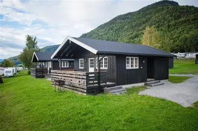 a small black cabin with a green field and a mountain at Pluscamp Mageli in Bjørge