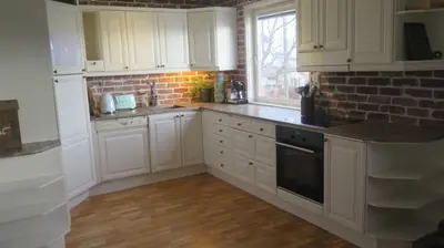 a kitchen with white cabinets and a brick wall at Sara's Fjord View House in Stadlandet