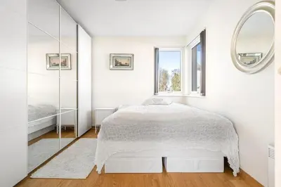 a white bedroom with a bed and a mirror at A cozy three bedroom apartment for rent in Heimdal