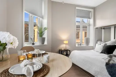 a bedroom with a bed and a table and two windows at Roomsly - Cozy Hilltop Hideout in Central Bergen in Bergen