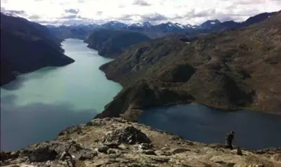 a person standing on top of a mountain overlooking a lake at Ski in & out hytte på Lemonsjøen i Jotunheimen in Randsverk