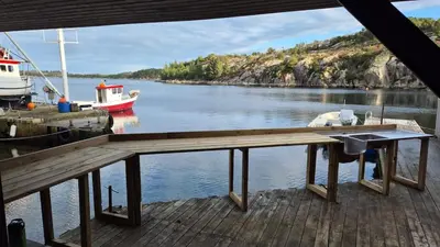 a dock with a table and a boat in the water at cozy house with boat dock, sauna - FJORDTID in Rubbestadneset