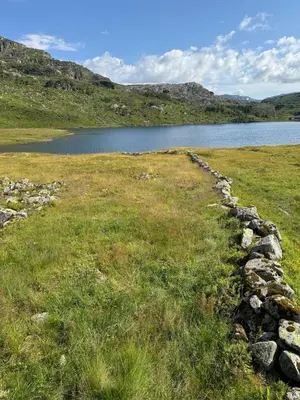 a stone wall in a field next to a lake at Wild Norwegian nature, between Preikestolen & Trolltunga in Sauda
