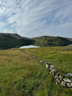 a stone wall in a field next to a body of water at Wild Norwegian nature, between Preikestolen & Trolltunga in Sauda