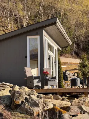 a small black cabin with a porch and some rocks at Fjord Cabin with Panoramic View & Private Balcony in Luster