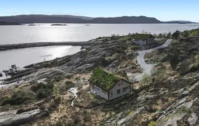 a house with a green roof on a hill next to the water at Cozy Home In Masfjordnes With Sauna in Masfjorden