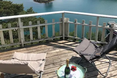 a deck with two chairs and a table with a bottle of wine at Seaside Cabin with panoramic view in Bømlo