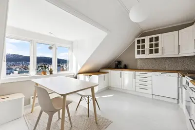 a kitchen with white cabinets and a table and chairs at Rom i loftsleilighet med utsikt in Bergen