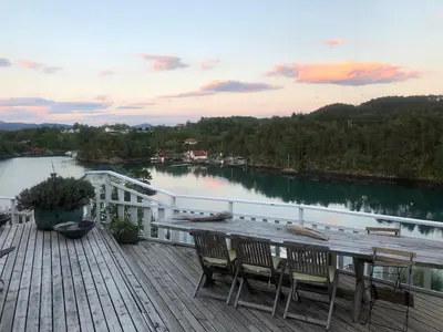 a deck with a table and chairs and a lake at Stay where the mountains begin in Bømlo
