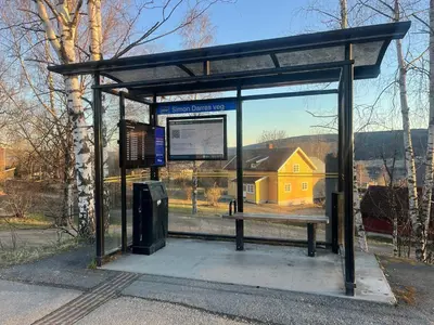 a bus stop with a bench and a yellow building at Leilighet i Lillehammer med gratis parkering in Lillehammer