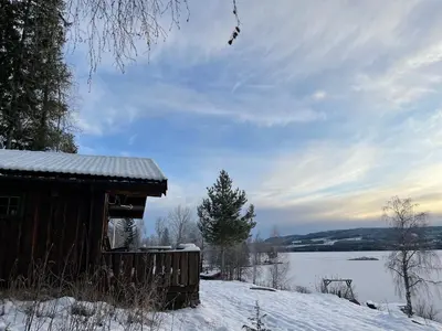a cabin in the snow next to a body of water at Hagali by Norgesbooking - cabin by the lake Næra, close to Sjusjøen in Ringsaker