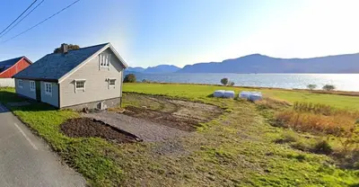a small house in a field next to a body of water at Gamlemgarden by Norgesbooking - house by the sea in Longva