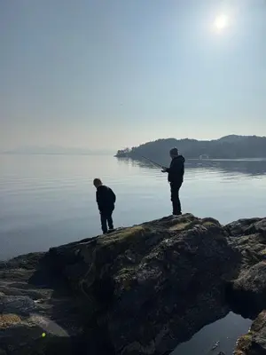 two men standing on a rock fishing in the water at Large villa with boathouse in Lunde