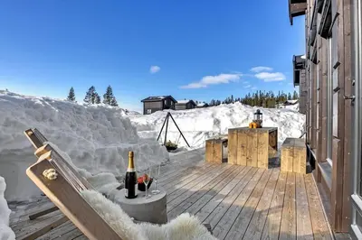 a deck in the snow with a bottle of wine at New, cozy cottage on Norefjell with stunning views in Noresund