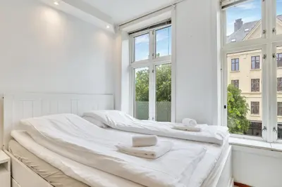 a white bedroom with two beds and a window at Fløyen Apartments in Bergen