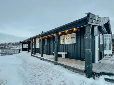 a cabin with a wooden deck in the snow at Idyllic Cabin By The Water In Hessdalen in Ålen