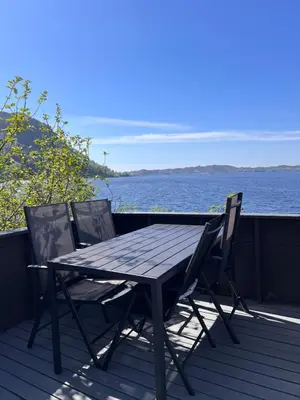 a wooden table and two chairs on a deck with the water at En Perle ved Masfjorden in Masfjorden