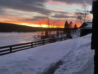 a fence in the snow with the sunset in the background at Atmospheric Log Cabin By Myllavannet