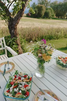 a white picnic table with a salad and flowers on it at Historic Croft With Views Over Lake Mjøsa in Ottestad