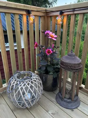 a porch with a lantern and flowers on a deck at Old Farmhouse Retreat with jacuzzi and sauna in Eidsvoll