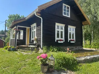 a black house with flowers in front of it at Old Farmhouse Retreat with jacuzzi and sauna in Eidsvoll