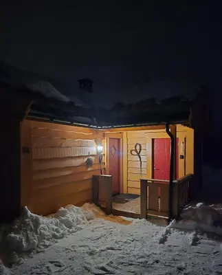 a house with a red door in the snow at night at Adventurous cabin cozy on Sjusjøen with sauna! in Sjusjøen