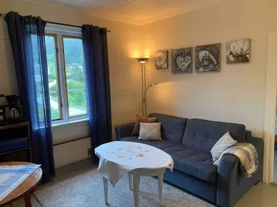 a living room with a blue couch and a table at Seaside apartment in farmhouse close to nature in Husevåg