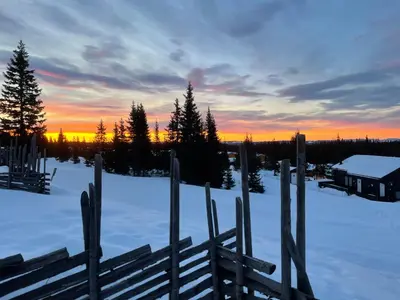 a fence in the snow with a sunset in the background at Modern mountain cabin Ski in-out 2 Bathrooms in Ringsaker