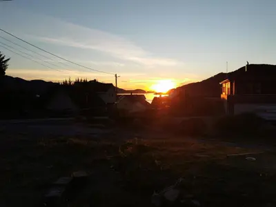 a sunset over a house with the sun setting at Fjordgløtt in Blålia