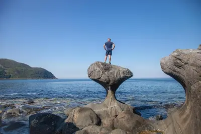 a man standing on a rock in the ocean at Idyllisk overnatting i dome ved sandstrand in Langenes
