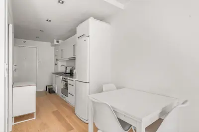 a white kitchen with a table and a white refrigerator at Bergen Beds Apartment I Right Behind Bryggen! in Bergen