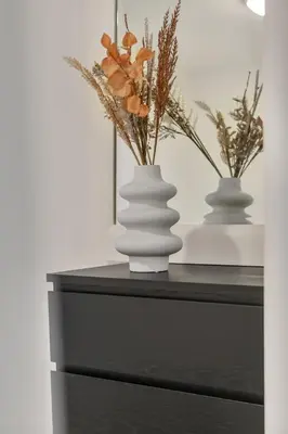 two white vases with flowers on a black dresser at Bryggen Gateway Homes in Bergen
