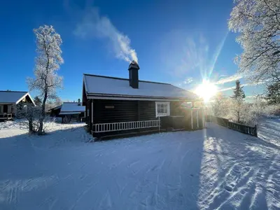 a house in the snow with the sun behind it at Log Cabin With Mountain View in Beitostøl