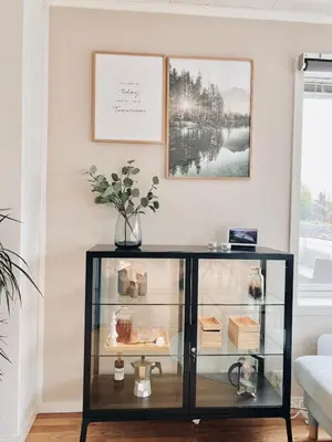 a glass display cabinet in a living room with a picture on the wall at 2BR, 2 parking spots, EV-charger and home office in Trondheim