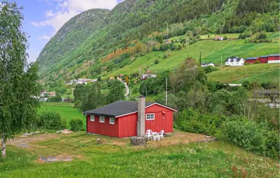a red house in a field with mountains in the background at 1 Bedroom Awesome Home In Vik I Sogn in Vikøyri